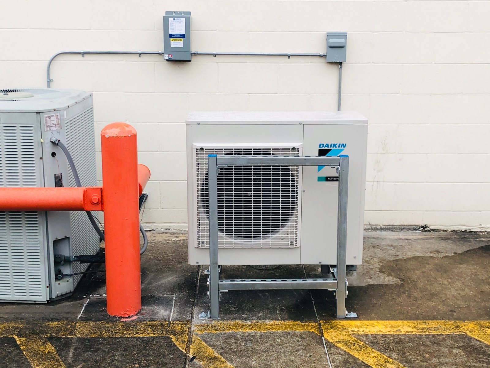 Daikin condenser on a Unistrut stand and guard frame next to a bollard at a Houston self-storage drive aisle