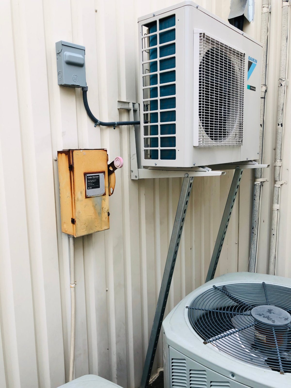 Daikin inverter condenser wall-mounted on Unistrut supports above an existing condenser at a Houston self-storage facility