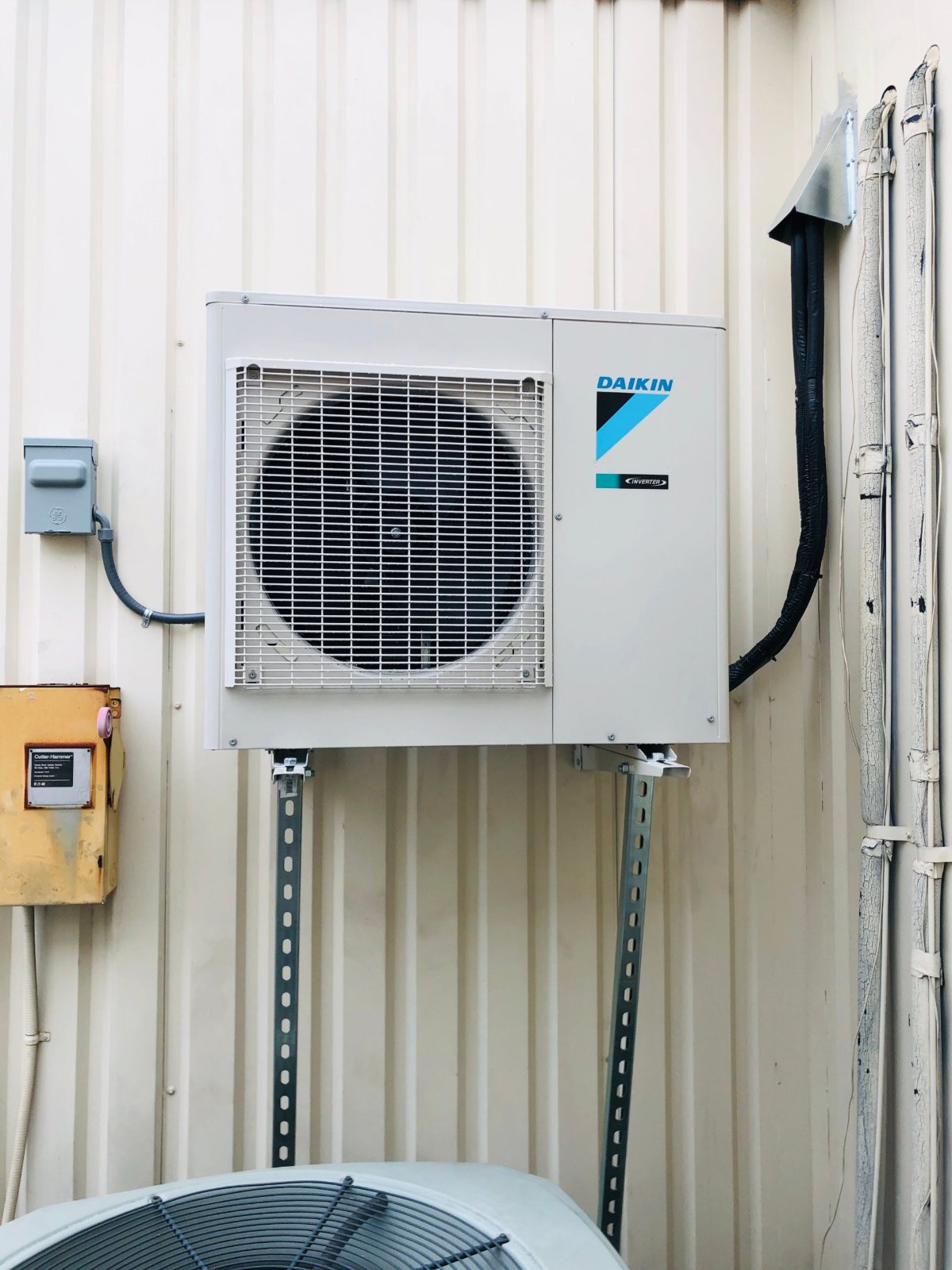 Front view of a wall-mounted Daikin condenser with new disconnect and line set for an elevator machine room in Houston