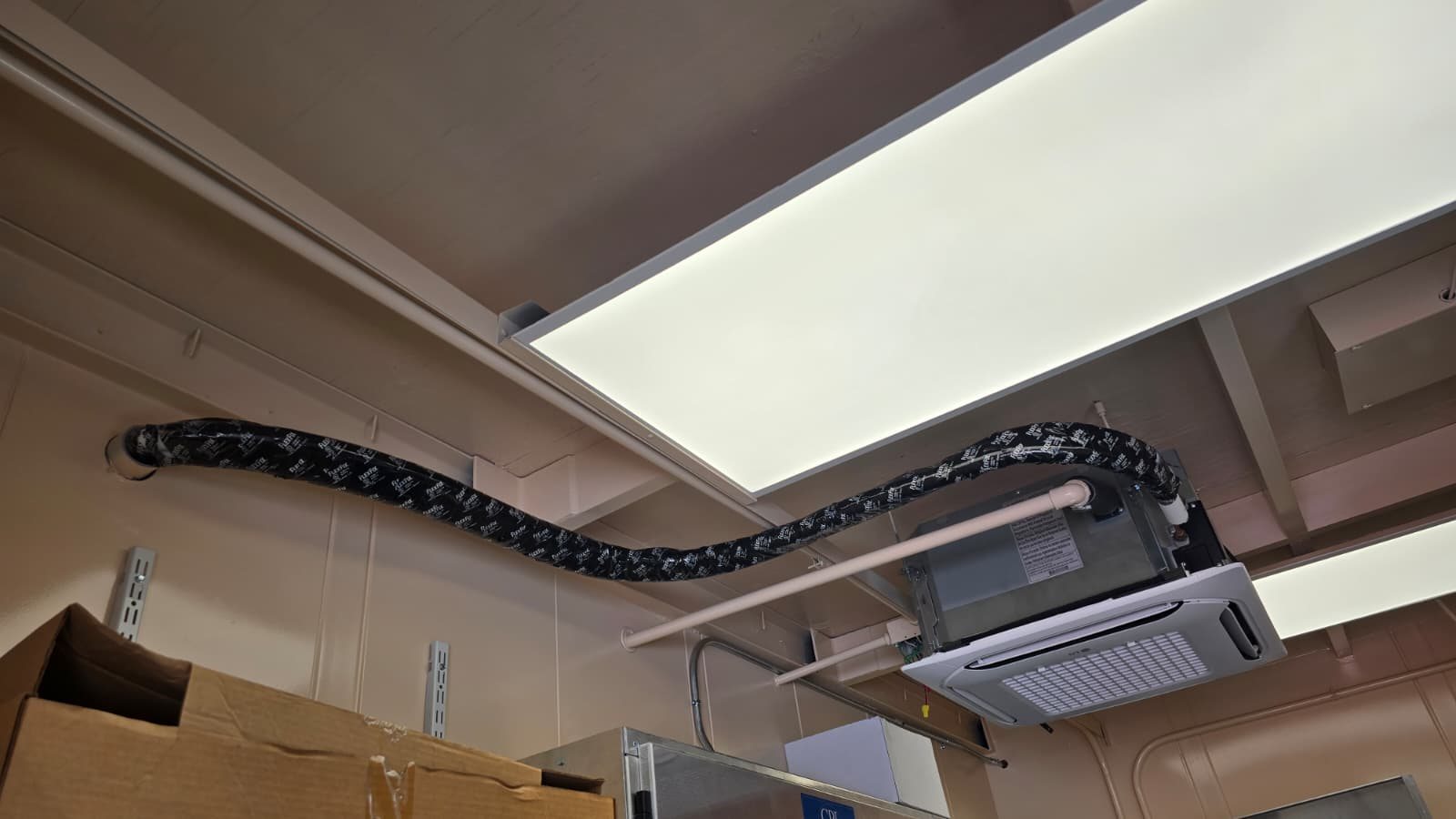 Insulated refrigerant line set run across the ceiling to an LG cassette inside a fuel station data hut