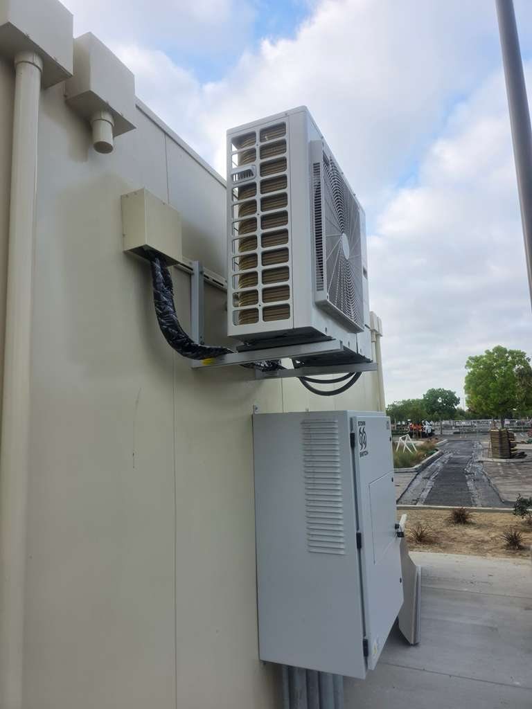 Side view of wall-mounted LG condenser with line set cover and electrical box at a fuel station data hut