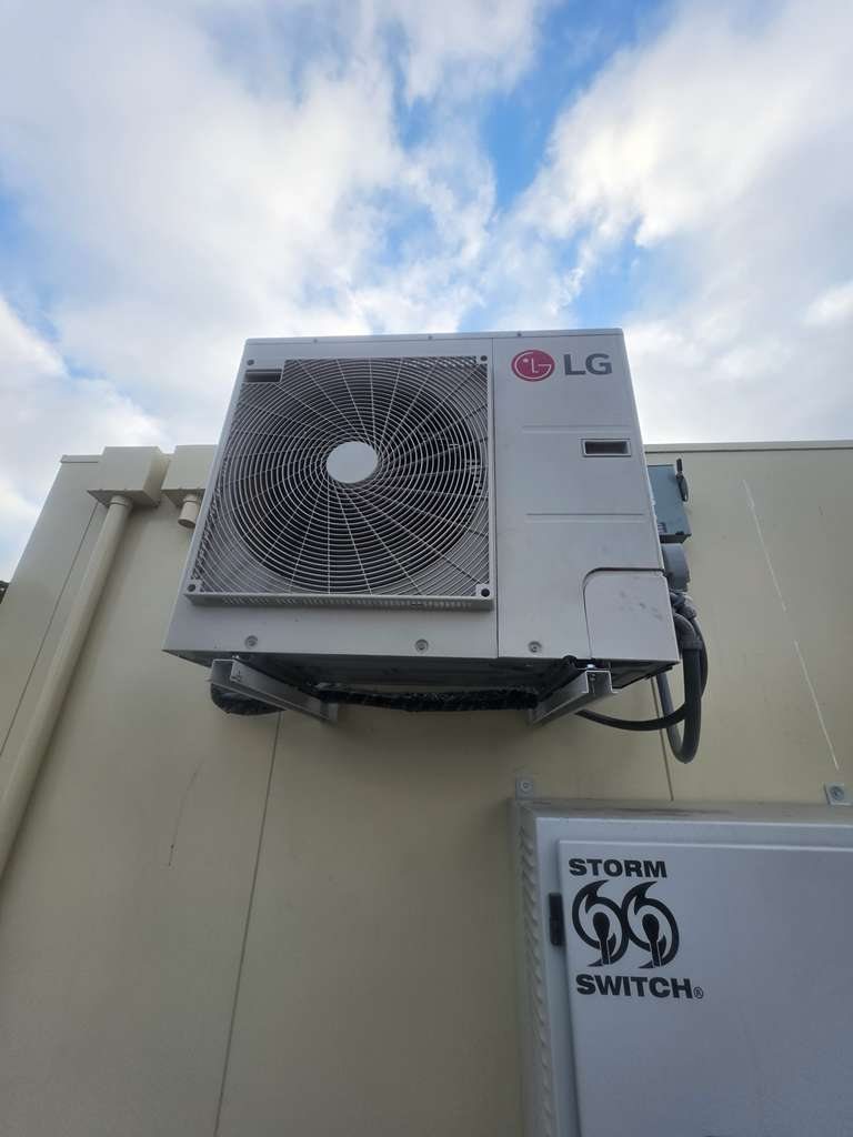 LG outdoor unit mounted on wall brackets above the generator transfer switch at a fuel station data hut