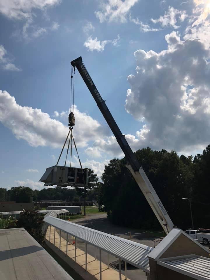 Crane setting a rooftop HVAC unit over a commercial building walkway