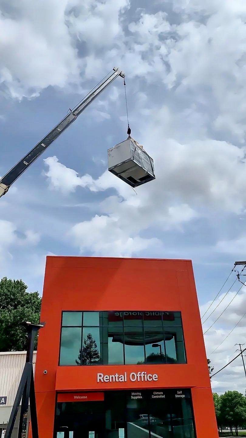 Rooftop HVAC unit lifted by crane over a self-storage rental office
