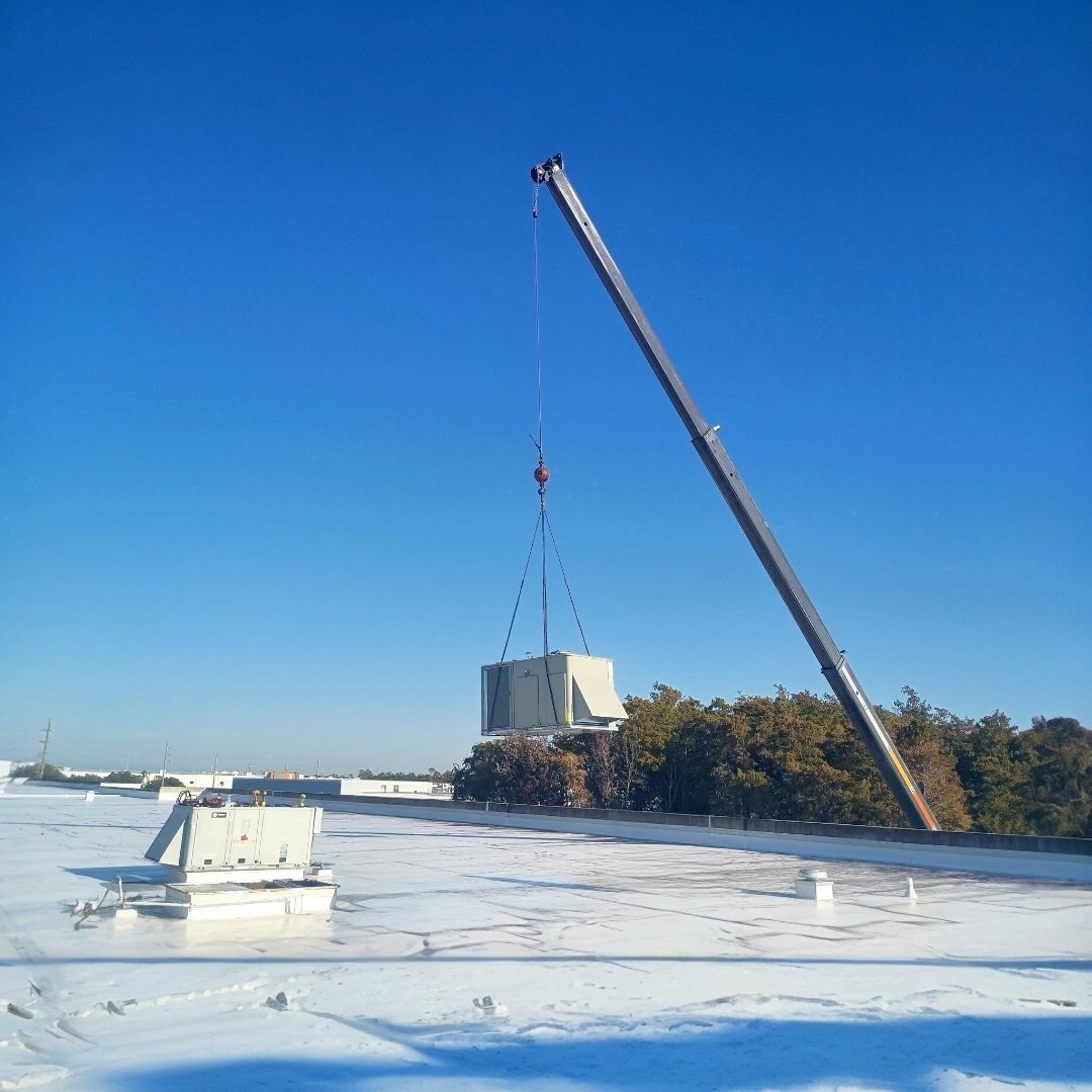 Crane lifting a new rooftop HVAC unit onto a white commercial roof