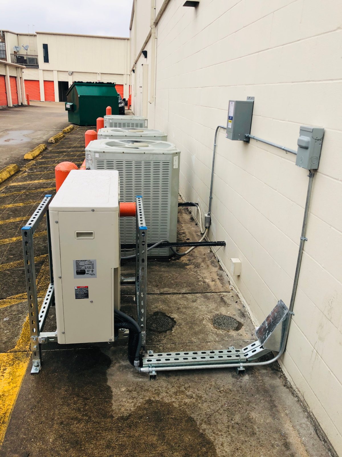 Daikin ductless condenser on a galvanized Unistrut stand beside existing units along a self-storage drive aisle in Houston